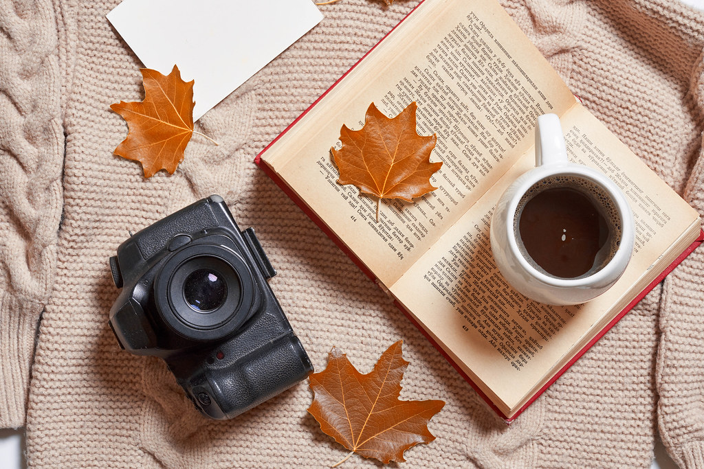 Fall leaves, warming sweater, cup of coffee, book and photo camera