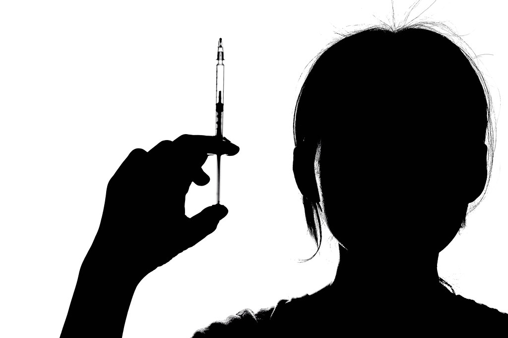 Female doctor silhouette holding up a syringe with a vaccine