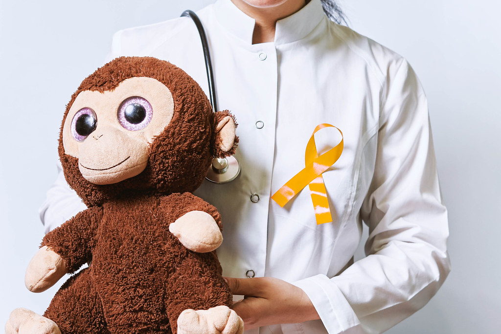 Female doctor with pinned Childhood cancer day yellow ribbon holding a kid's plush toy