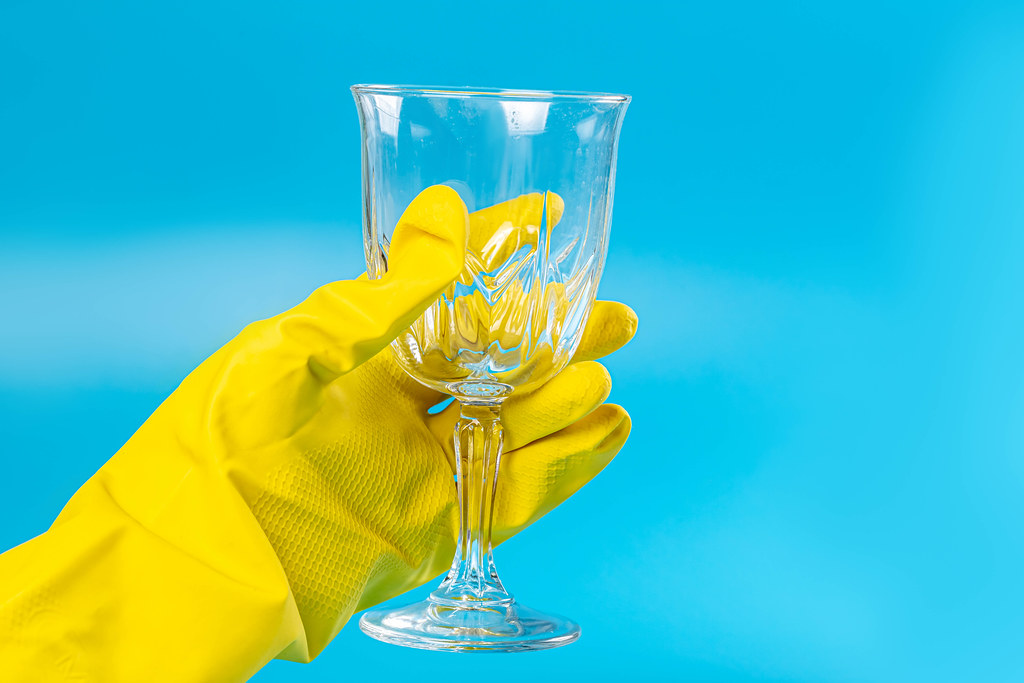 Female hand in a rubber glove holds a wine glass on a blue background