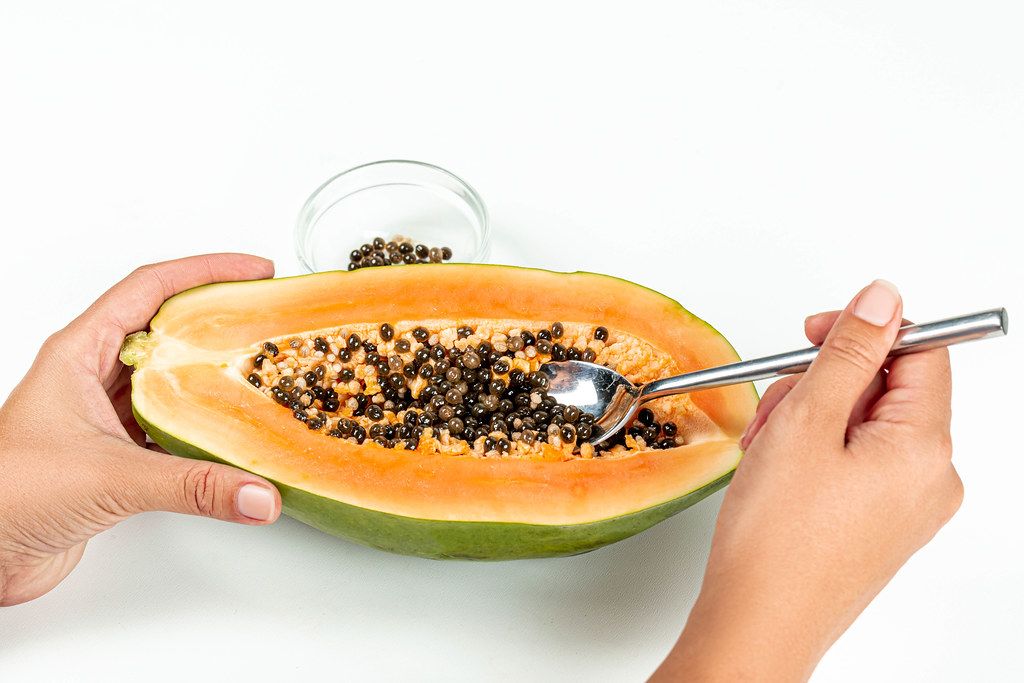 Female hands clean papaya from seeds with a spoon
