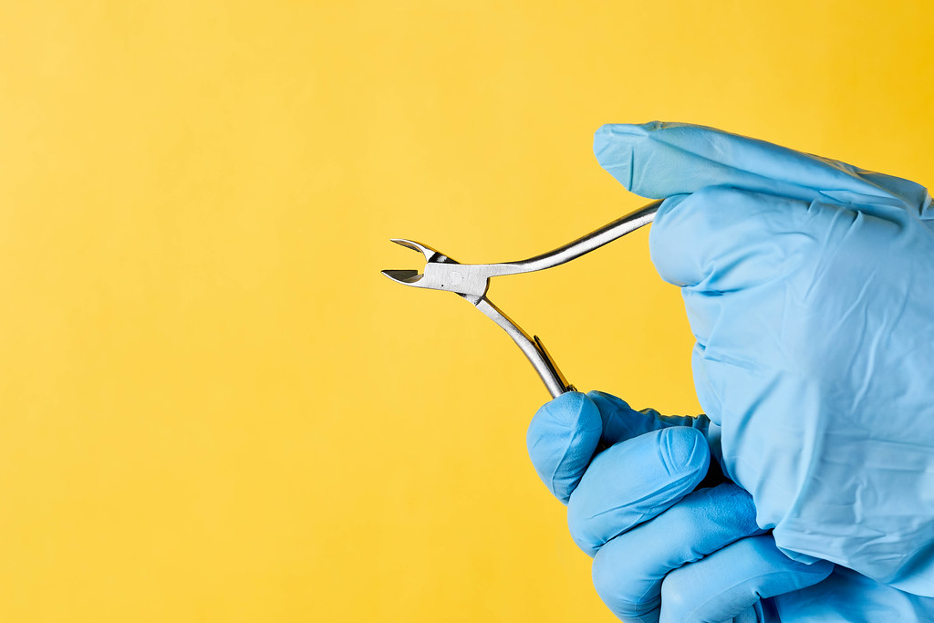 Female hands hold cuticle nipper over yellow background