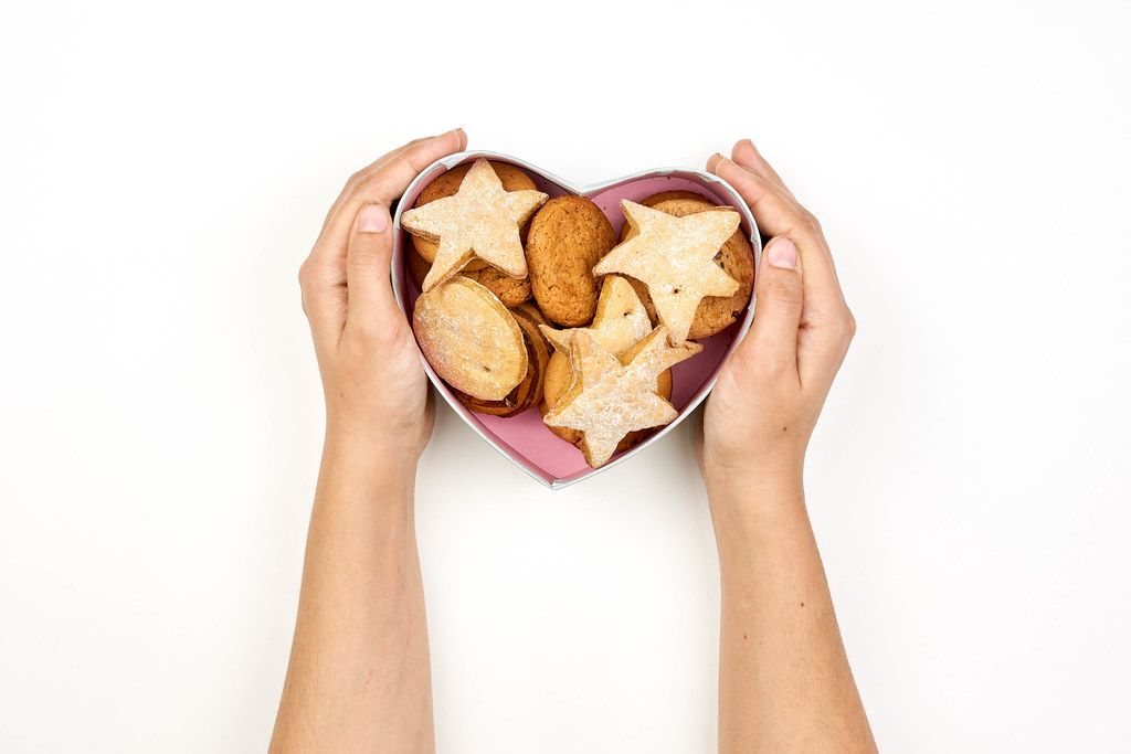 Female hands holding heart-shaped box with sweet cookies
