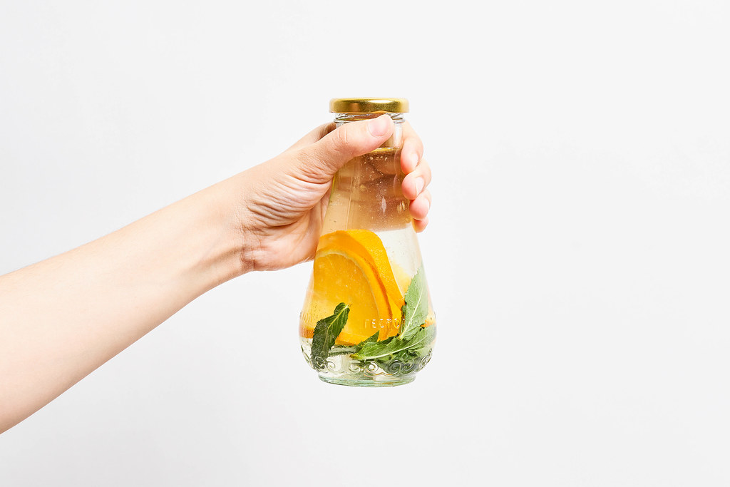 Female holds a glass bottle of infused water with lemon and mint