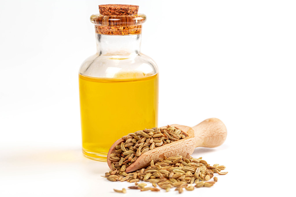 Fennel seeds with essential oil in a bottle over white background