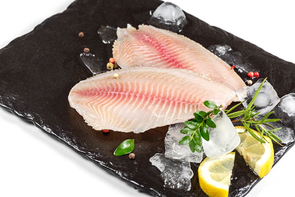 Fillet of tilapia fish with ice cubes on a black stone tray