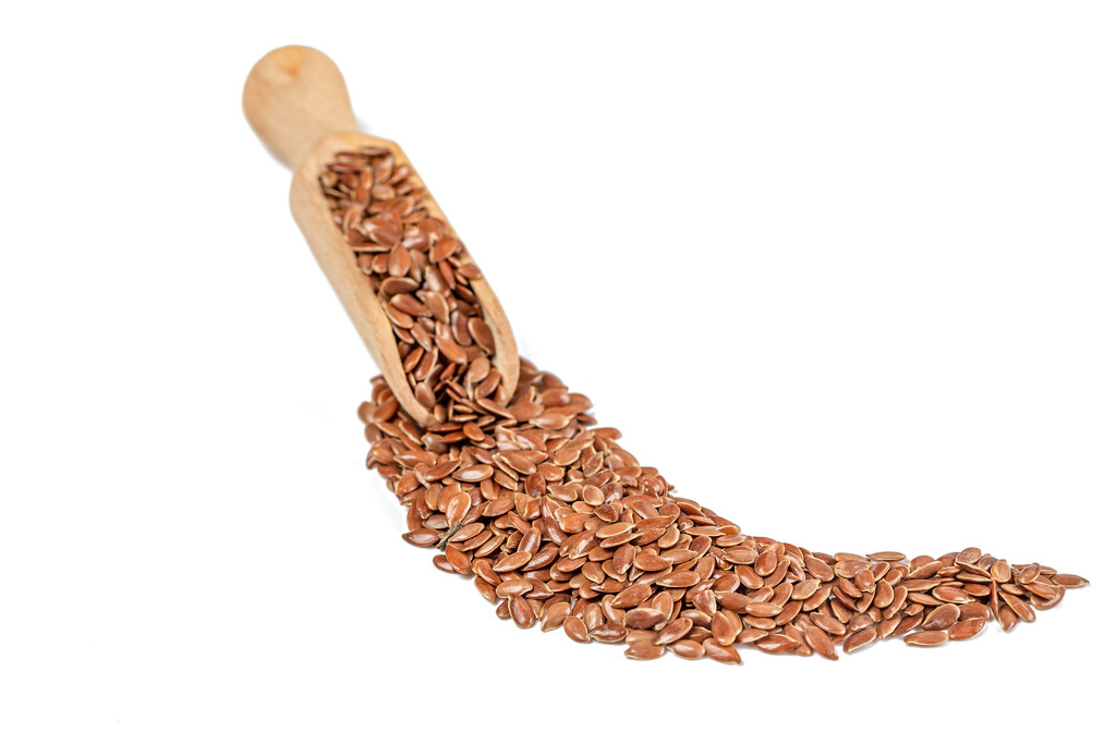Flax seeds in wooden scoop on white background
