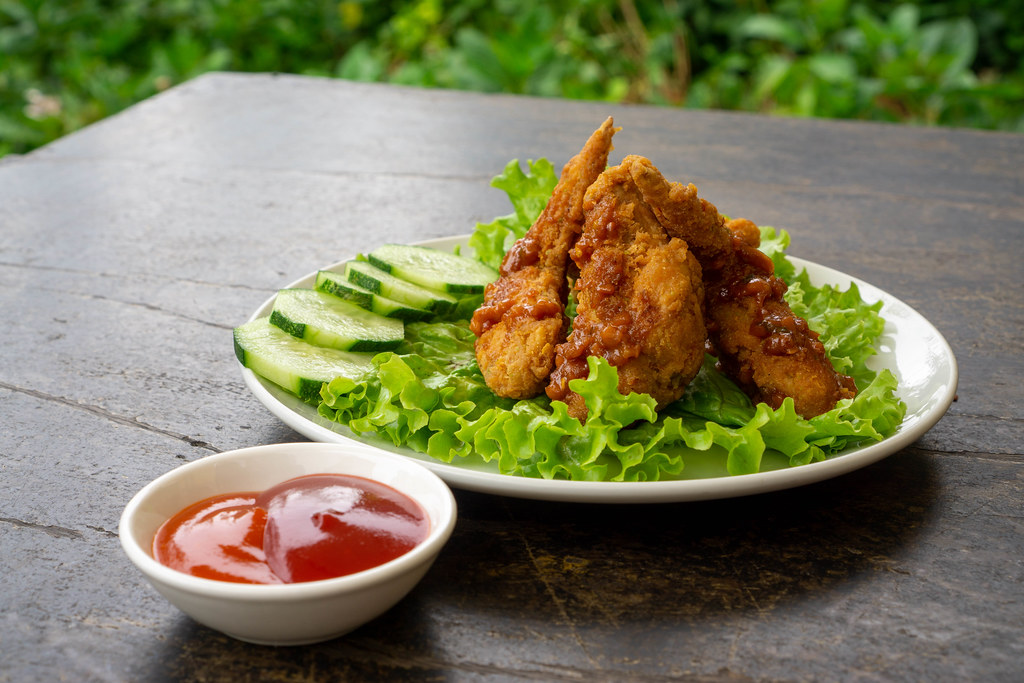 Food Photo of Fried Chicken Wings with Cucumber Slices and Lettuce on a Wooden Table with Tomato Ketchup and Chili Sauce