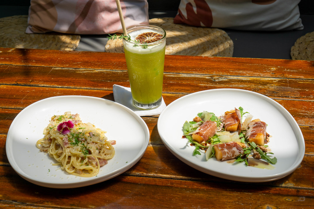 Food Photo of Healthy Fruit Juice in a Glas on a Wooden Table with Spaghetti Carbonara as Main Dish and Honeydew Melon wrapped in Parma Ham with Arugula and Parmesan Cheese as Appetizer