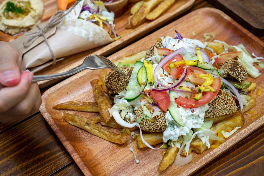 Food Photo of Person using Fork to eat Vegetarian Kapsalon Salad with French Fries, Homemade Falafel, Fresh Vegetables and Tzatziki Sauce for Lunch