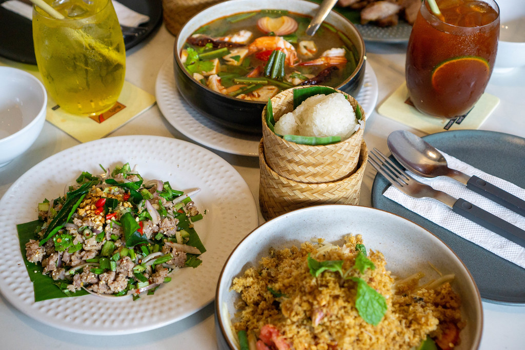 Food Photo of popular Thai Dishes such as Tom Yum Soup, Papaya Salad and Pad Gra Prow with Iced Green Tea and Lemon Tea in a Restaurant