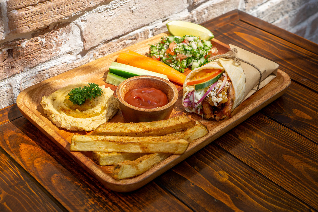 Food Photo of Sun shining on a Restaurant Lunch Meal with Doner Kebab Chicken Wrap, Homemade French Fries, Hummus Dip, Raw Vegetables and Quinoa Salad on a Wooden Plate