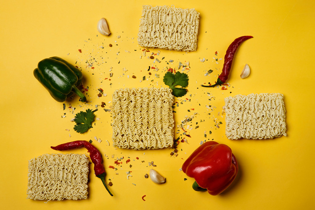 Four dry instant noodles blocks with vegetables and spices on vibrant yellow background