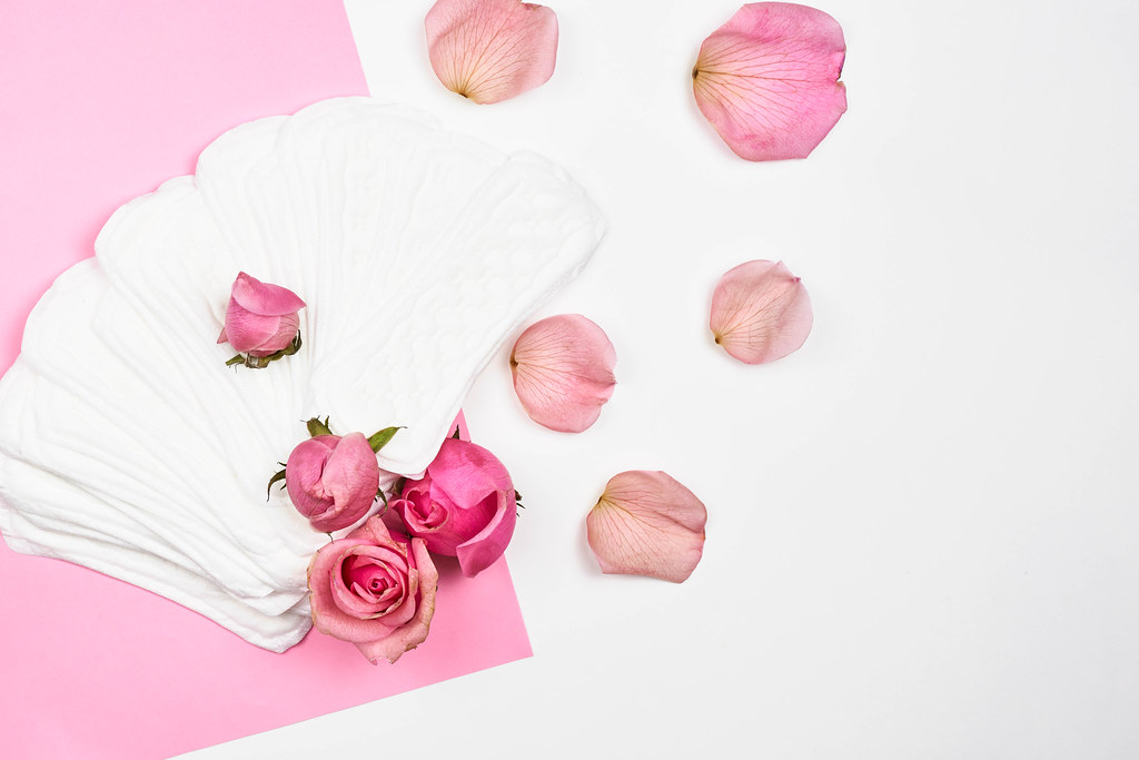 Frauen-Hygieneartikel: lose Slipeinlagen und Rosen auf rosa-weißem Hintergrund mit Platz für Text