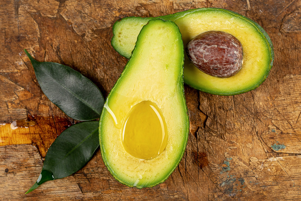 Fresh halves of ripe avocado with oil and leaves