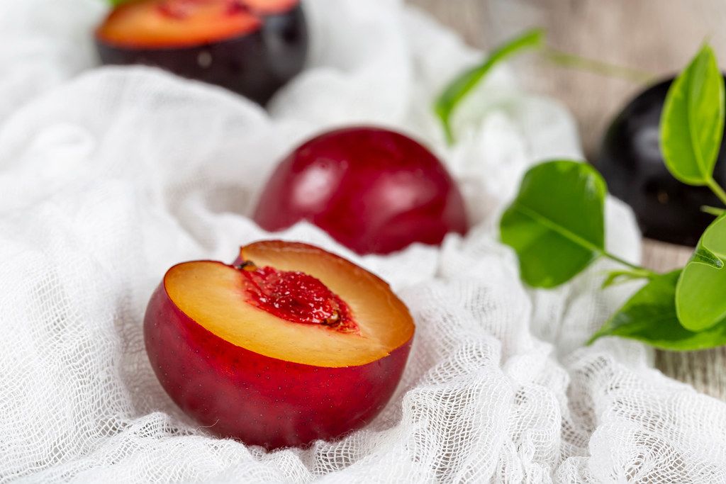 Fresh juicy plum half on a wooden background with white gauze
