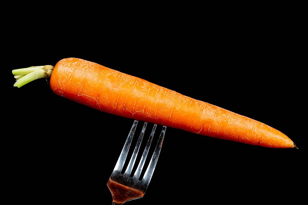 Fresh raw carrot on a fork on a black background
