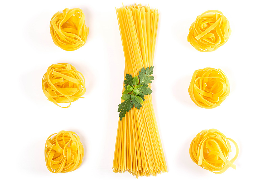 Fresh uncooked fettuccine pasta and spaghetti with with basil and parsley on a white background