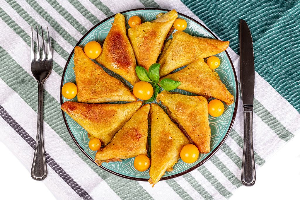 Fried pancakes with minced meat in the form of triangles with yellow tomatoes, top view
