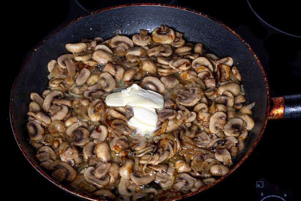 Frying pan with fried mushrooms, onions and butter on a hob
