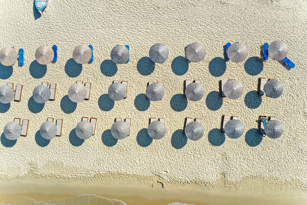 Geometric beach design: overhead drone shot of rows of thatched beach umbrellas at Plaka, Naxos
