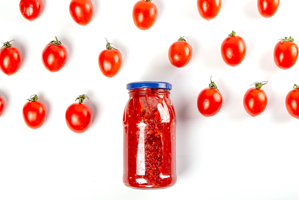 Glass jar with tomato sauce and fresh tomatoes on a white background