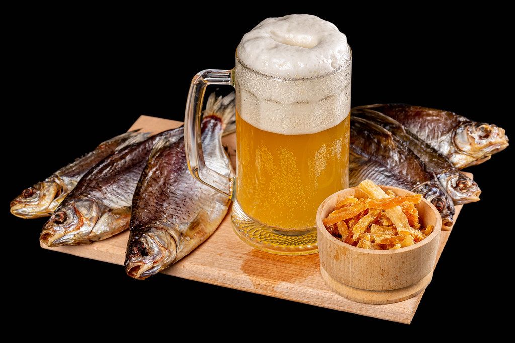 Glass of beer with dried fish on a dark background
