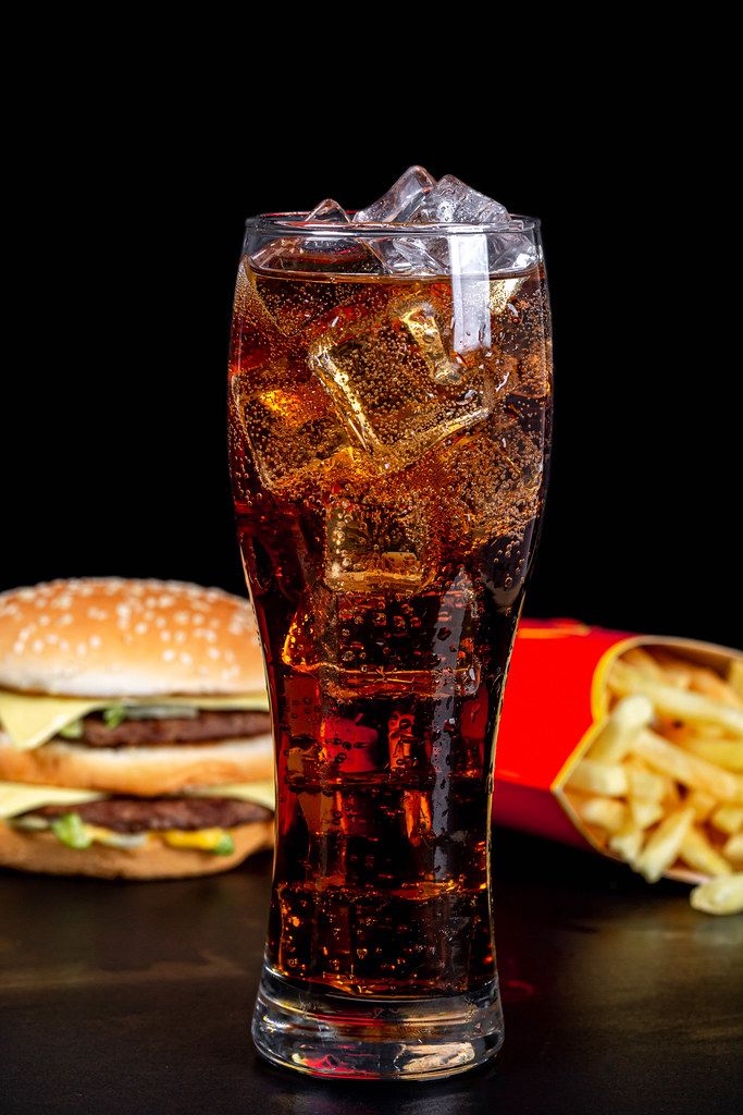Glass of cold coca cola on a dark background with fries and burger