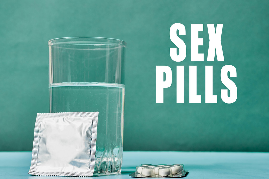 Glass of water, medicines and condom on table. Sex pills