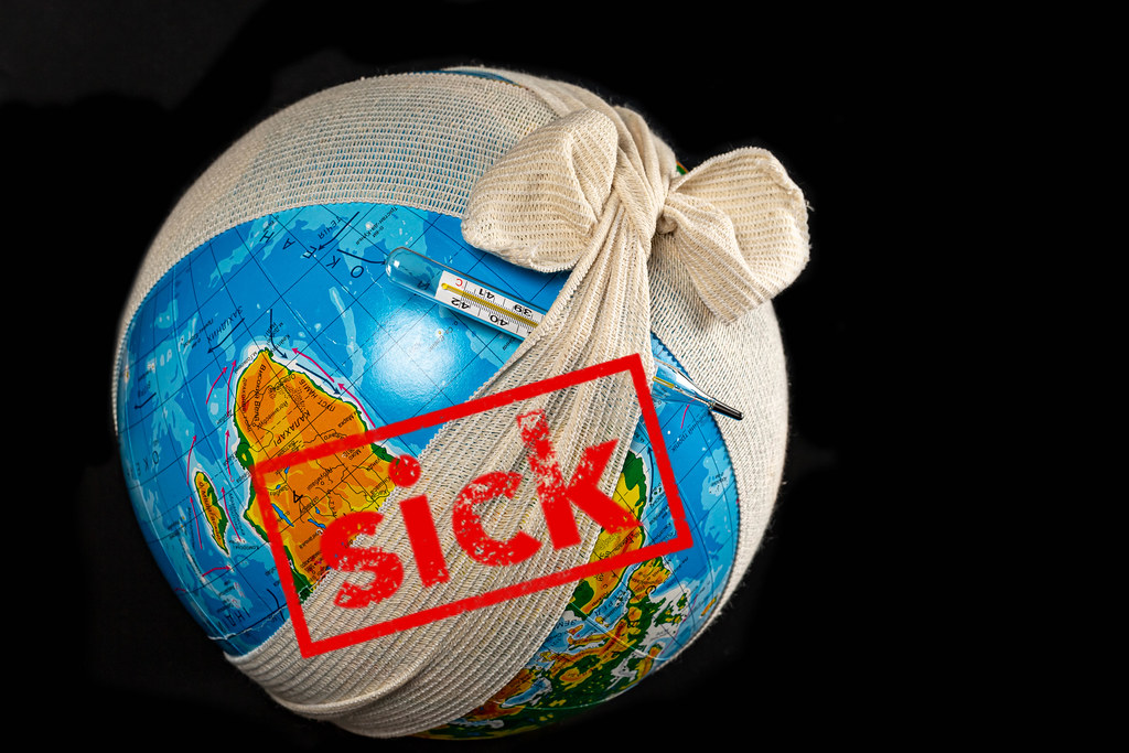 Globe in a bandage with an elastic bandage with a thermometer on a dark background, the concept of the planet is sick
