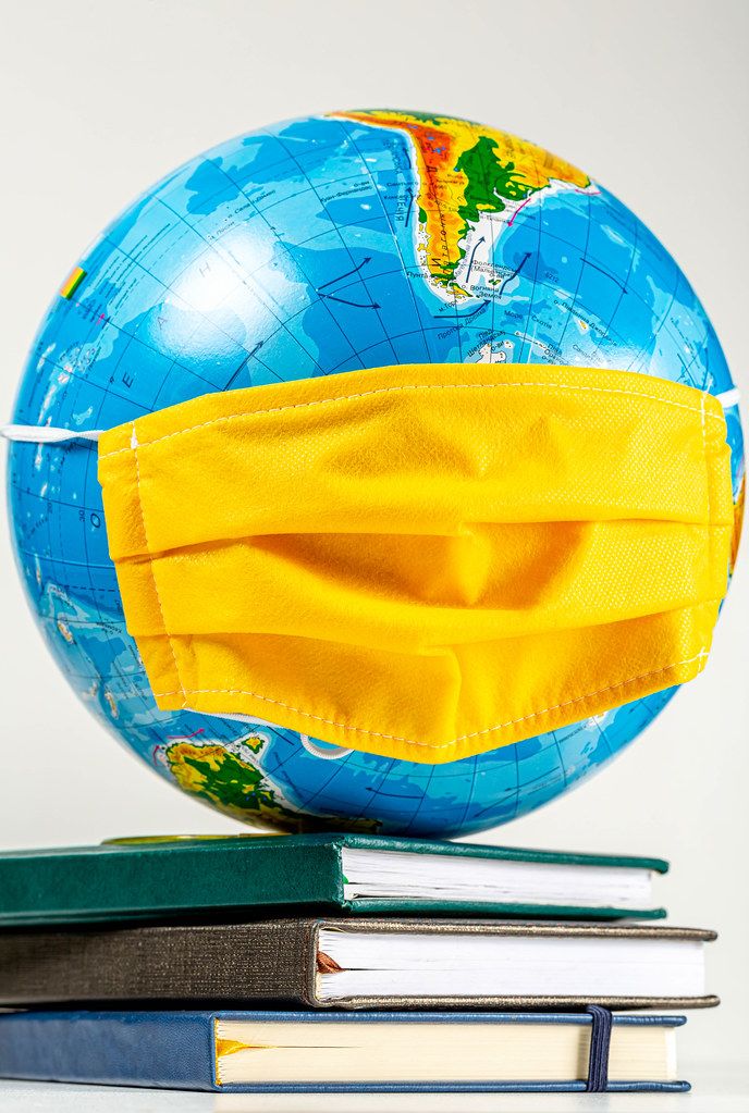 Globe in a yellow medical mask on a stack of books