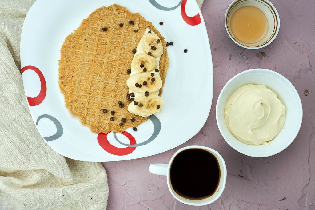 Gluten-free banana oat waffles with bowl of cream, honey and coffee cup