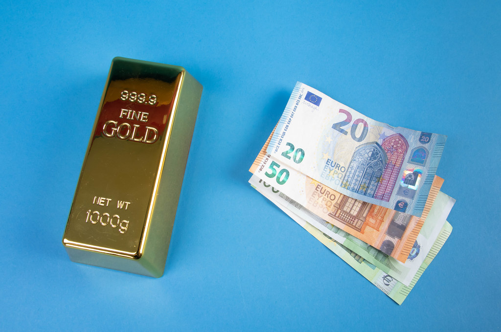 Gold brick with Euro banknotes on blue background