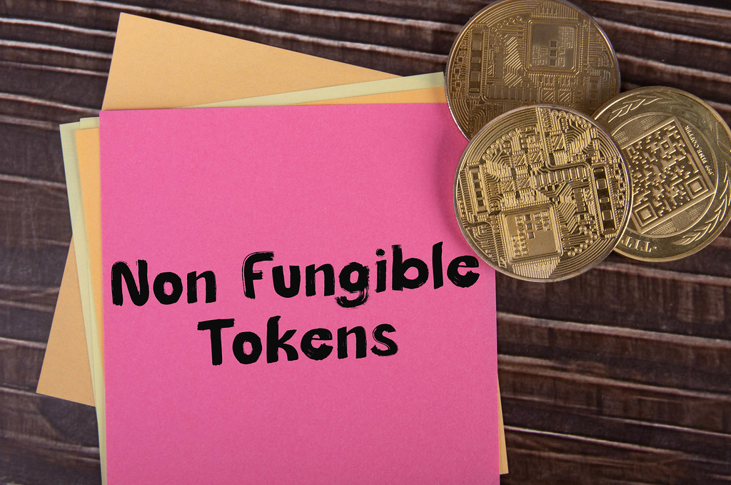 Golden coins and sticky notes with Non Fungible Tokens text on wooden table