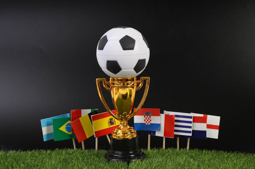 Golden trophy and ball with national flags on grass