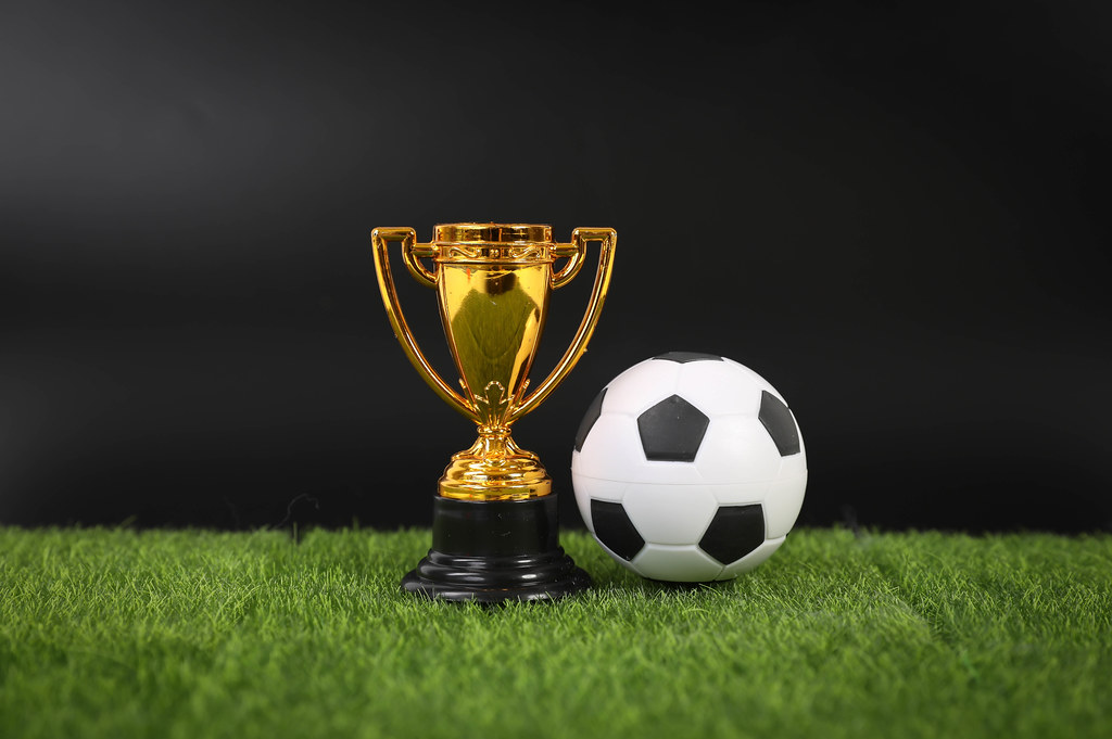 Golden trophy and football ball on grass