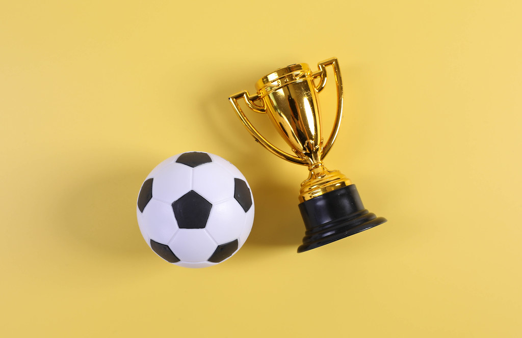 Golden trophy and football ball on yellow background