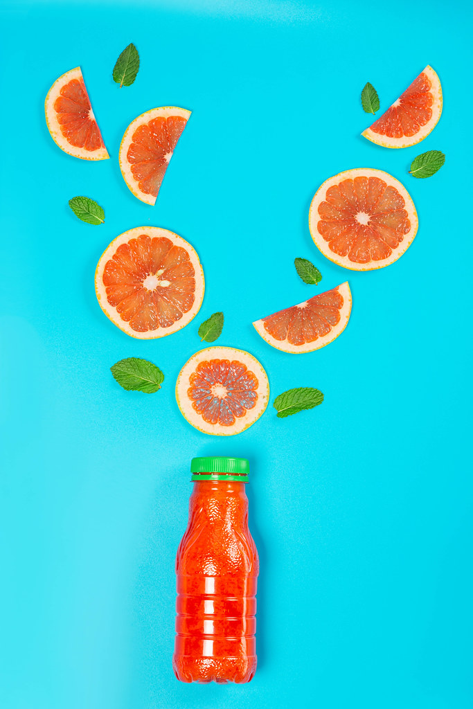 Grapefruit juice bottle with grapefruit pieces and fresh mint leaves on blue background