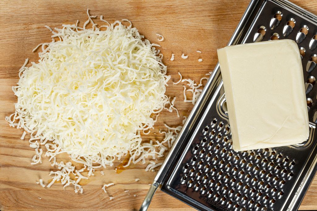 Grated mozzarella cheese, slab of cheese and metal cheese grater, top view