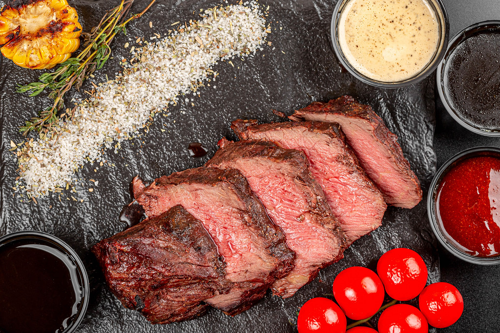 Grilled beef steak pieces on black background with spices and sauces