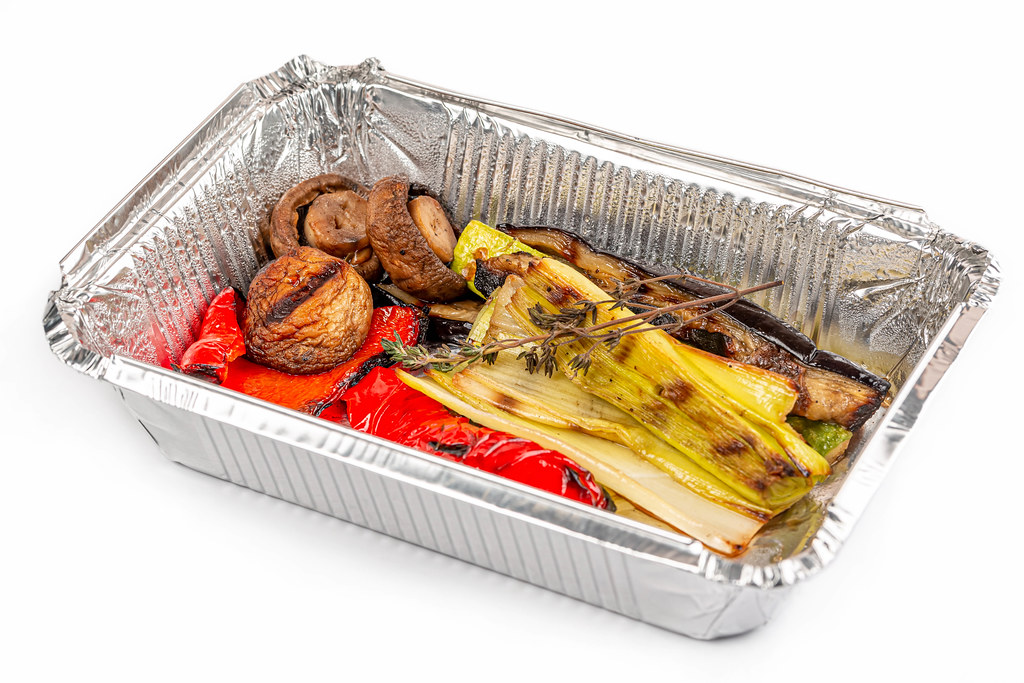Grilled vegetables in a foil container on a white background