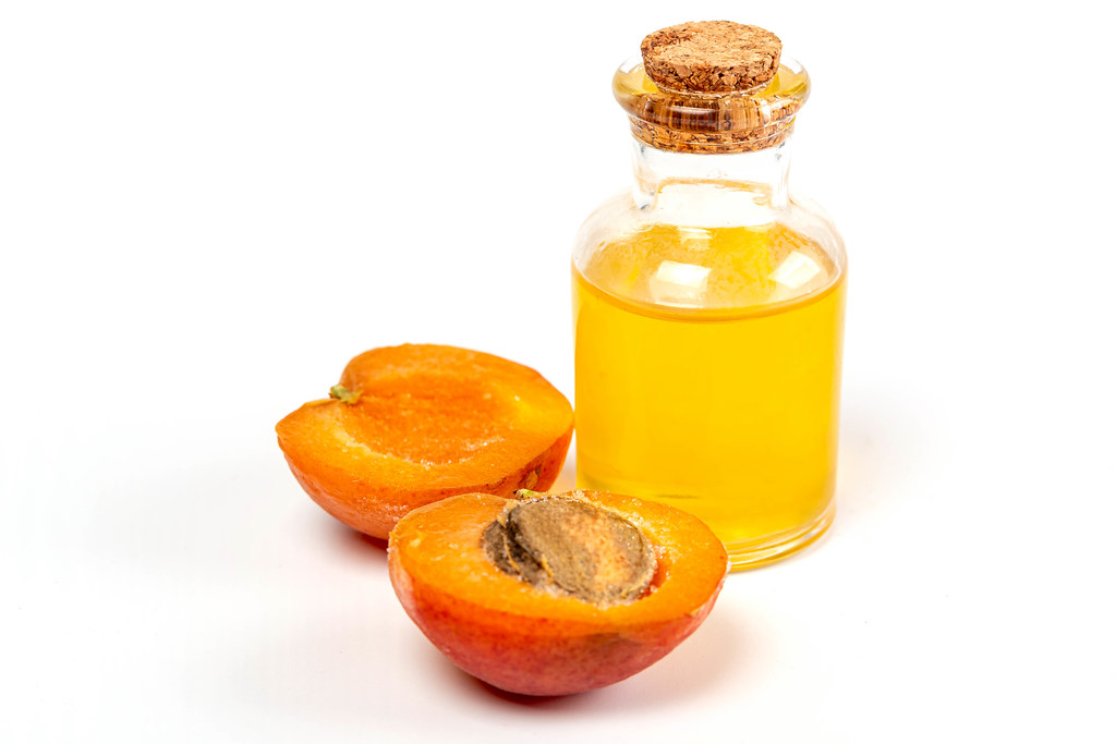 Halves of a ripe apricot and a bottle of oil on a white background