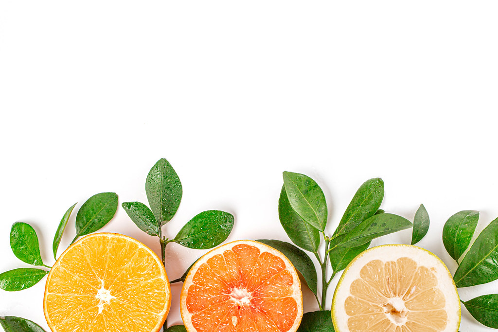 Halves of fresh citrus fruits with branches and green leaves, top view
