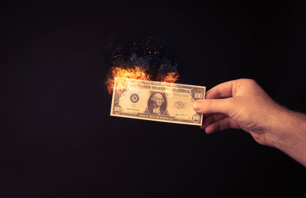 Hand holding 100 dollar banknote on fire