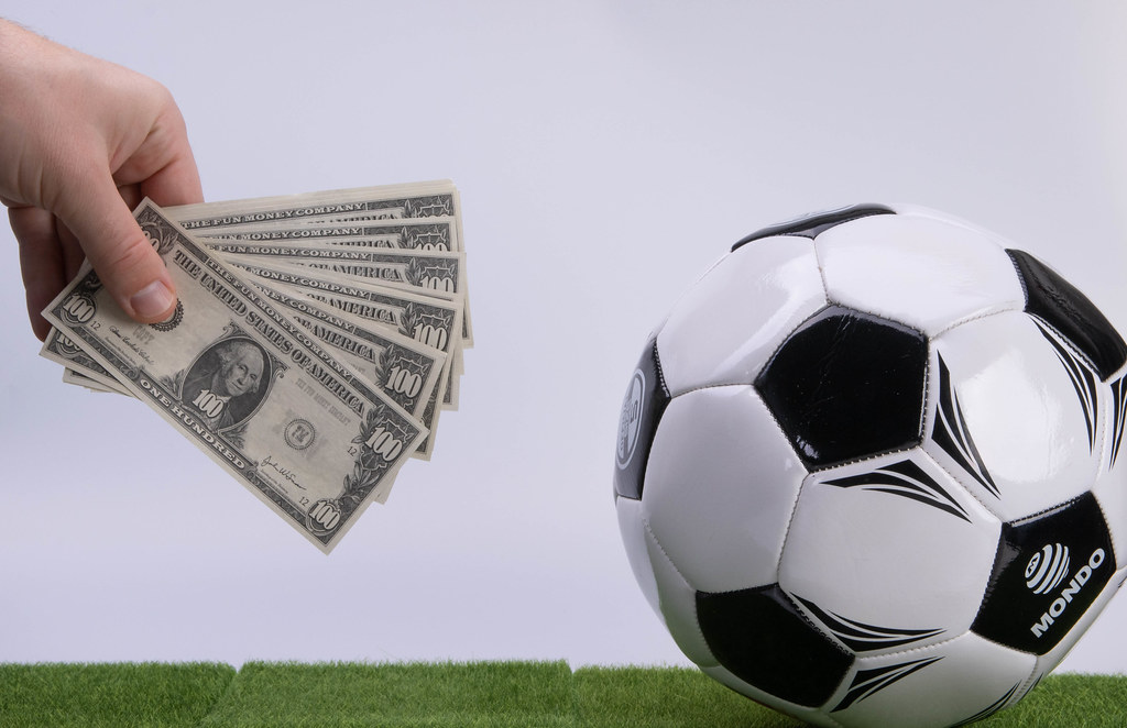 Hand holding 100 Dollars banknotes and soccer ball on white background