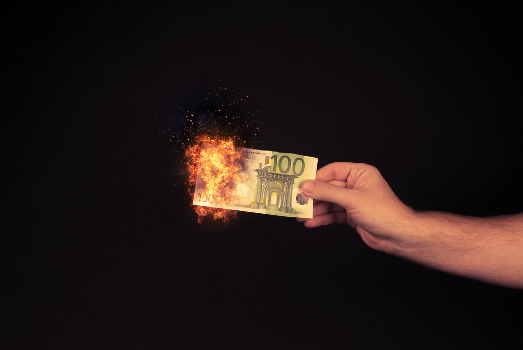 Hand holding 100 Euro banknote on fire on black bakground