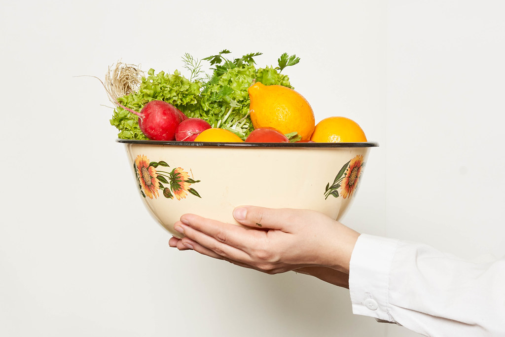 Hand holding a big bowl full with fresh fruits and vegetables