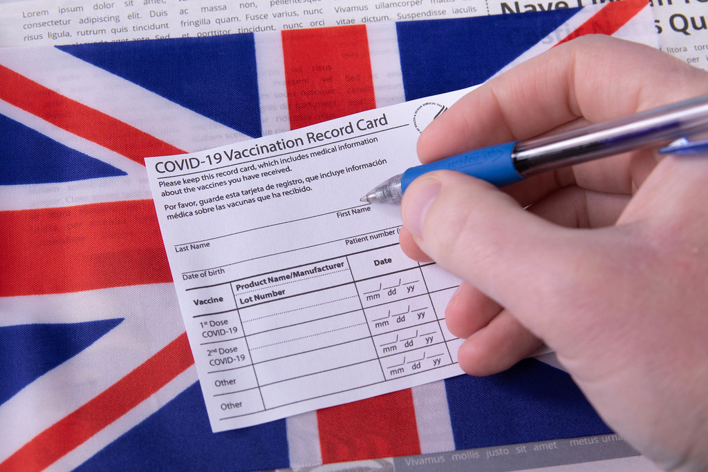 Hand holding a pen and Vaccination record card with flag of United Kingdom