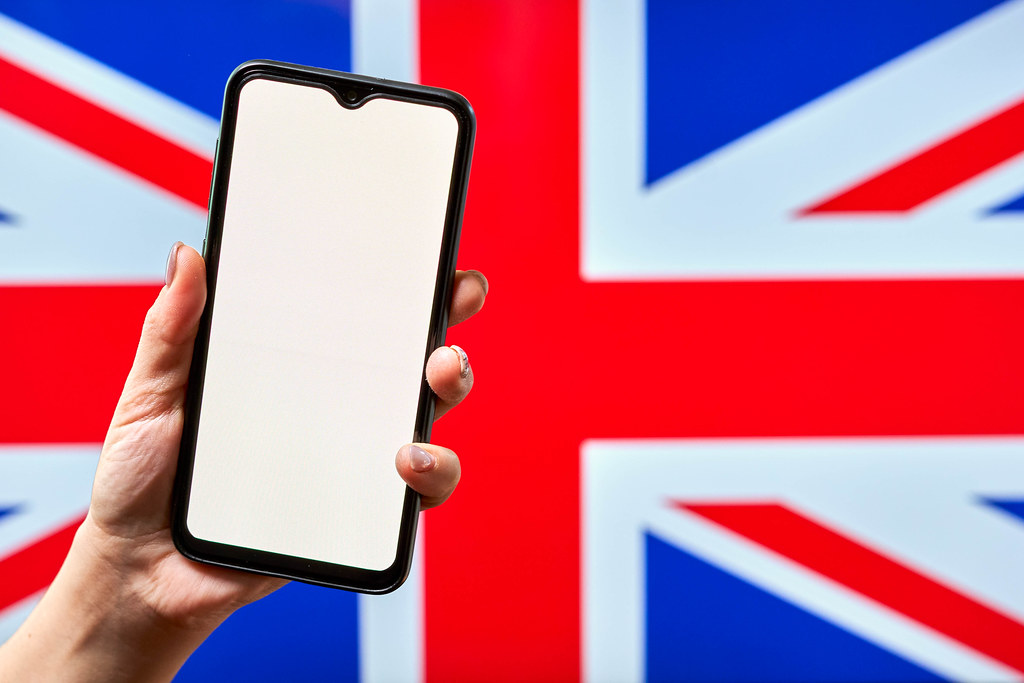 Hand holding a smartphone with a blank screen against the British flag
