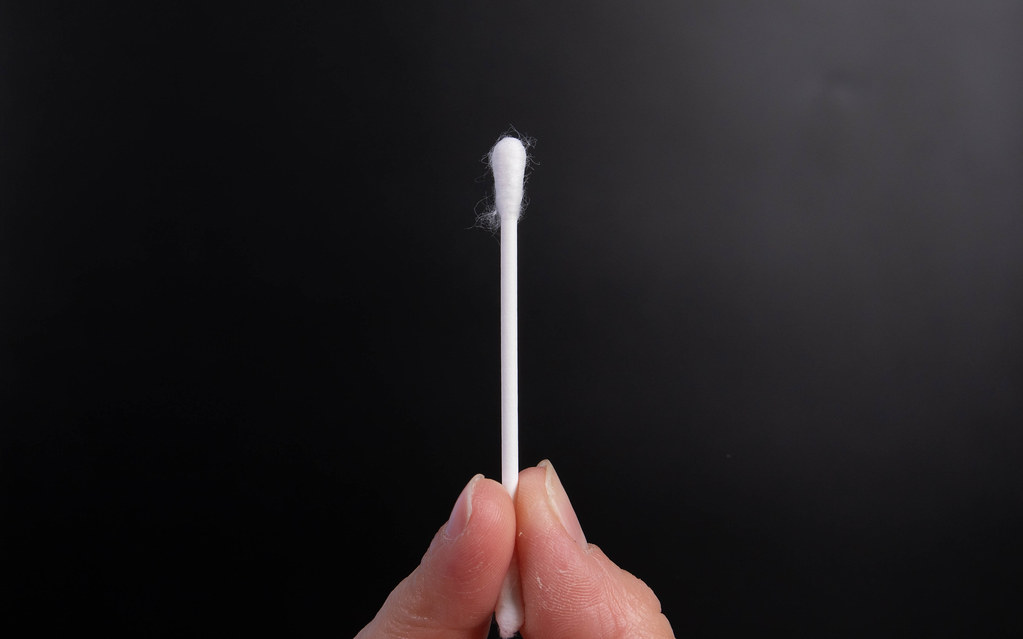 Hand holding cotton swab on a black background